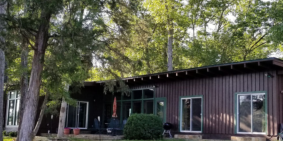 Lakeside exterior of Guntersville Getaway single-level home with covered patio and large windows facing the water