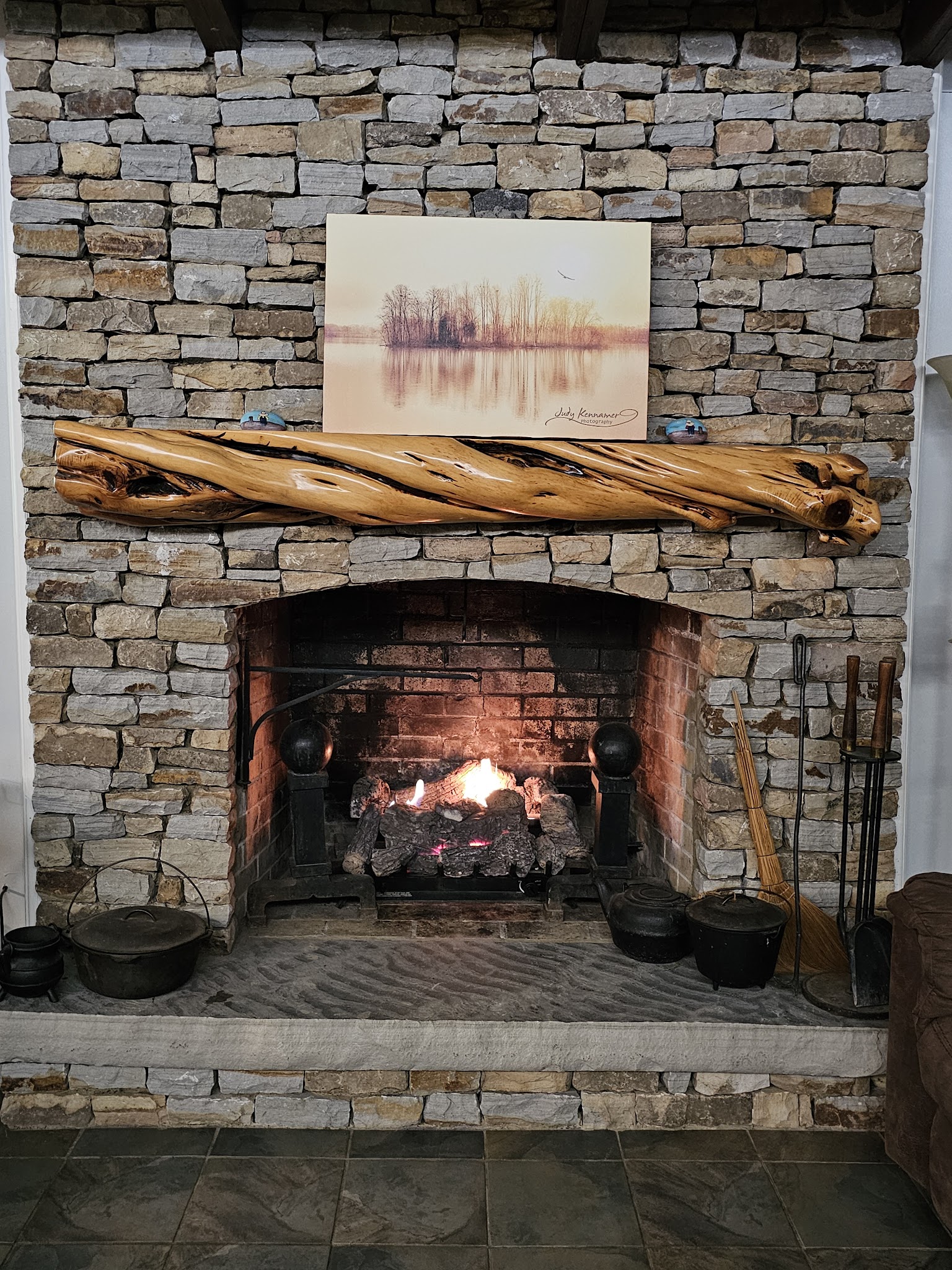 Stone fireplace with driftwood mantel and fire burning at Guntersville Getaway lake house